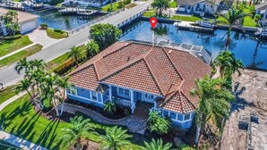 A house with a red-tiled roof, surrounded by a swimming pool, palm trees, and a dock. - Large corner lot home with canal views & screened in pool - close to the beach (Marco Island)