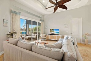 A spacious living room with a large sofa, a television, and a ceiling fan. - Large corner lot home with canal views & screened in pool - close to the beach (Marco Island)