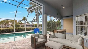 A poolside area with a sofa and chairs, a view of the pool, and a large window. - Large corner lot home with canal views & screened in pool - close to the beach (Marco Island)