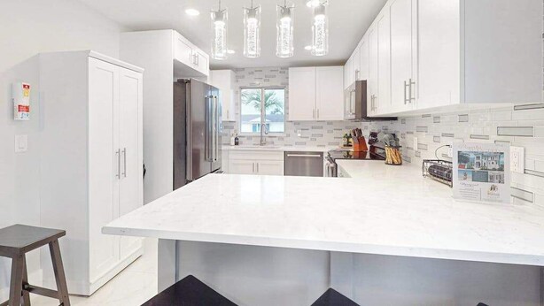 A modern kitchen with white cabinetry, a large island, pendant lighting, and a view of the outdoors. - Dog-friendly colorful condo with shaded patio, washer/dryer, & central AC (Naples)