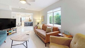 A modern living room with a flat-screen TV, a sofa, a coffee table, and a ceiling fan. - Dog-friendly colorful condo with shaded patio, washer/dryer, & central AC (Naples)