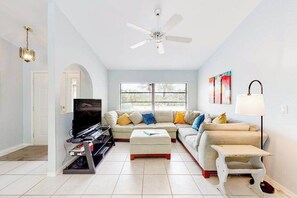 A living room with a TV, two sofas, a ceiling fan, and a window with blinds. - Dog-Friendly Pool Retreat with Lanai, Grill & Central Location (Port Charlotte)
