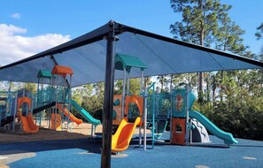Ein Spielplatz mit mehreren Rutschen und Klettergerüsten, beschattet von einer großen Markise.