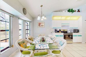 A dining area with a glass table, wicker chairs, and a kitchen in the background. - Dog-Friendly Pool Retreat with Lanai, Grill & Central Location (Port Charlotte)
