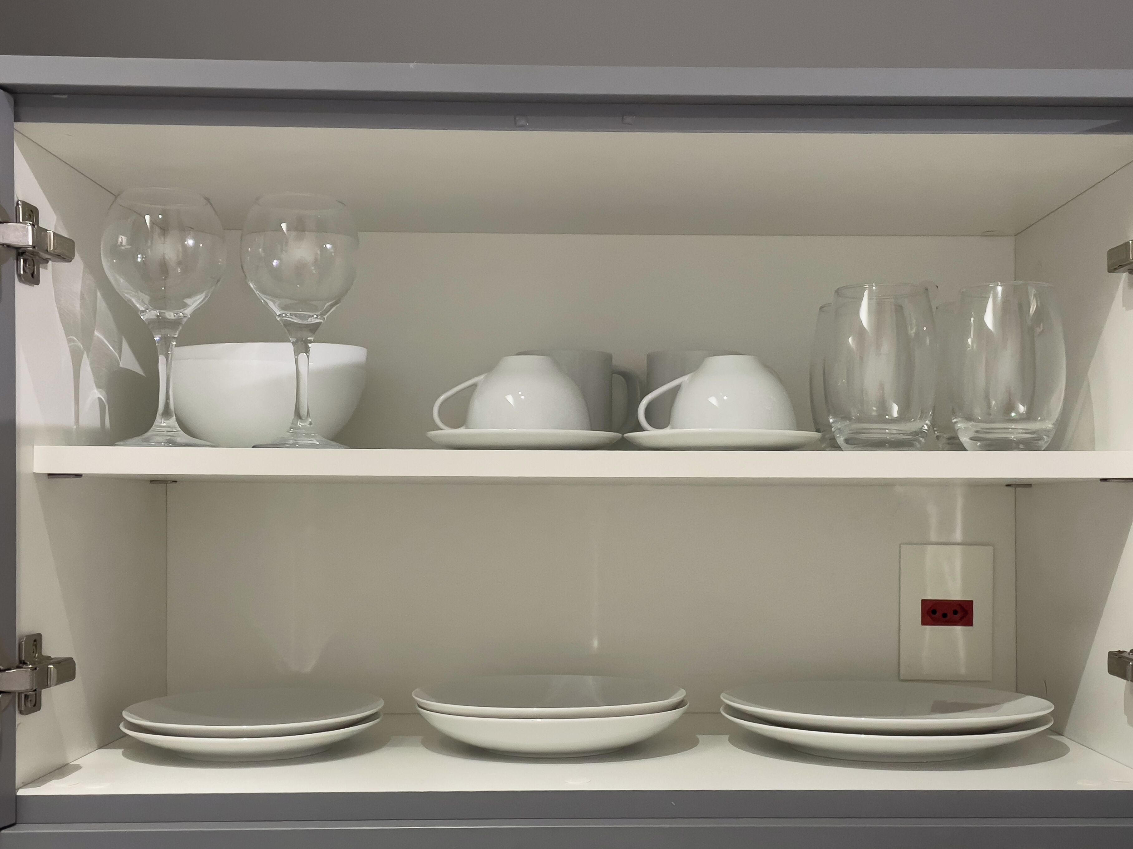 A white cabinet with shelves containing white glassware and bowls.