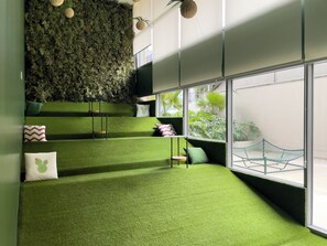 Un intérieur moderne avec un sol recouvert d’un gazon artificiel vert, un mur agrémenté d’un jardin vertical et une vue sur la verdure extérieure grâce à de grandes fenêtres.