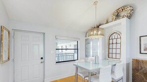 Un área de comedor con una mesa de vidrio y sillas blancas, una puerta blanca, un ventanal con vistas y un adorno mural.