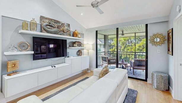 Una sala moderna con televisión de pantalla plana, sofá blanco y un balcón con mobiliario exterior.