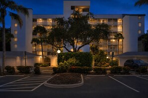 A multi-story hotel with a central courtyard, parking area, and a vehicle parked in the lot. - 3rd-floor snowbird-friendly condo with enclosed balcony, outdoor pool, W/D, AC (Naples)
