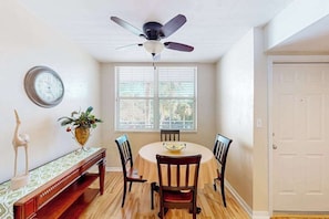 A dining area with a round table, four chairs, a ceiling fan, a clock on the wall, and a door to the right. - 3rd-floor snowbird-friendly condo with enclosed balcony, outdoor pool, W/D, AC (Naples)