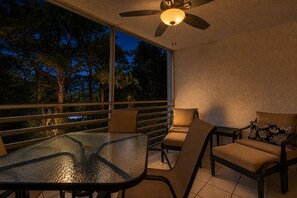 A balcony with a glass table, chairs, and a ceiling fan. - 3rd-floor snowbird-friendly condo with enclosed balcony, outdoor pool, W/D, AC (Naples)
