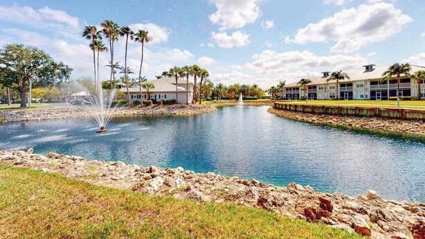 A hotel with a water feature, palm trees, and a clear sky. - Lakefront condo with pool, tennis, lake views, grill, patio, W/D, fast WiFi & AC (Naples)