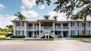 A two-story building with a central staircase, balconies, and a parking lot. - Lakefront condo with pool, tennis, lake views, grill, patio, W/D, fast WiFi & AC (Naples)
