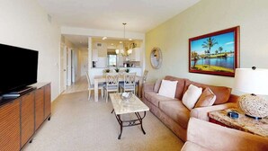 A living room with a TV, a sofa, a coffee table, and a dining area with chairs and a table. - Lakefront condo with pool, tennis, lake views, grill, patio, W/D, fast WiFi & AC (Naples)