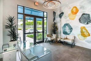A modern interior with a glass desk, two white chairs, and a wall with abstract art. - Contemporary condo with EV charger, central AC, & W/D - snowbird-friendly (Naples)