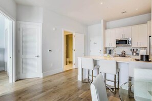A modern kitchen with white cabinets, a stainless steel microwave, and a glass dining table. - Contemporary condo with EV charger, central AC, & W/D - snowbird-friendly (Naples)