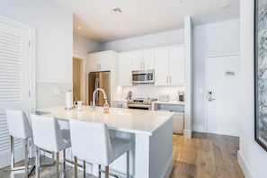 A modern kitchen with white cabinetry, stainless steel appliances, and a central island with bar stools. - Contemporary dog-friendly studio with central AC and washer/dryer (Naples)