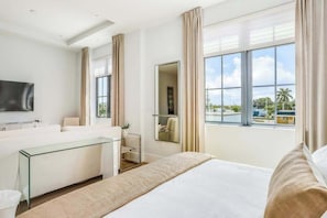 A hotel room with a bed, a glass desk, a TV, a mirror, and a window with a view of palm trees. - Contemporary dog-friendly studio with central AC and washer/dryer (Naples)