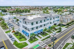 A multi-story building with a modern design, featuring a prominent entrance, a parking area, and a green space with palm trees. - Contemporary dog-friendly studio with central AC and washer/dryer (Naples)