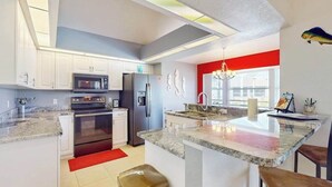 A modern kitchen with white cabinets, stainless steel appliances, a red accent wall, and a large island. - Close to Gulf with pool & updated interior (Rotonda West)
