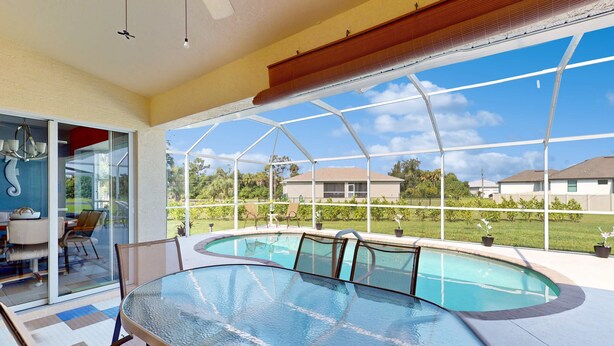 A glass-enclosed pool area with a table and chairs, a ceiling fan, and a view of the surrounding neighborhood. - Close to Gulf with pool & updated interior (Rotonda West)