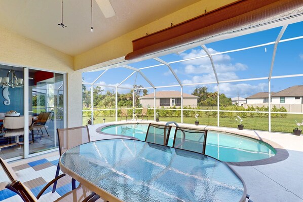 A glass-enclosed pool area with a table and chairs, a ceiling fan, and a view of the surrounding neighborhood. - Close to Gulf with pool & updated interior (Rotonda West)