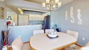 A dining area with a round table, white chairs, a chandelier, and a kitchen in the background. - Close to Gulf with pool & updated interior (Rotonda West)