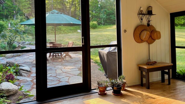 Une pièce dotée de grandes fenêtres, d’un patio en pierre, de mobilier d’extérieur et de plantes en pot.