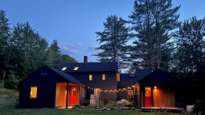Une maison moderne à deux étages, dotée d’une façade sombre, de grandes fenêtres et d’une entrée bien éclairée.
