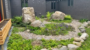 Un jardin agrémenté de rochers, de plantes et d’un bac à fleurs en bois.