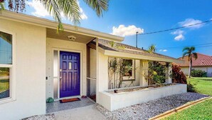 Una casa a un piano con una porta viola, un portico coperto e un piccolo giardino.