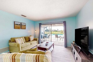 A living room with a sofa, a coffee table, a flat-screen TV, and a sliding glass door leading to a pool area. - Canal-front home with private pool, grill, patio, AC, W/D & gorgeous views (Rotonda West)