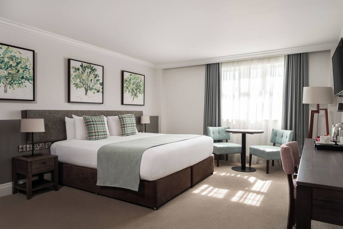 A hotel room with a large bed, bedside tables, a desk, a chair, and a TV.