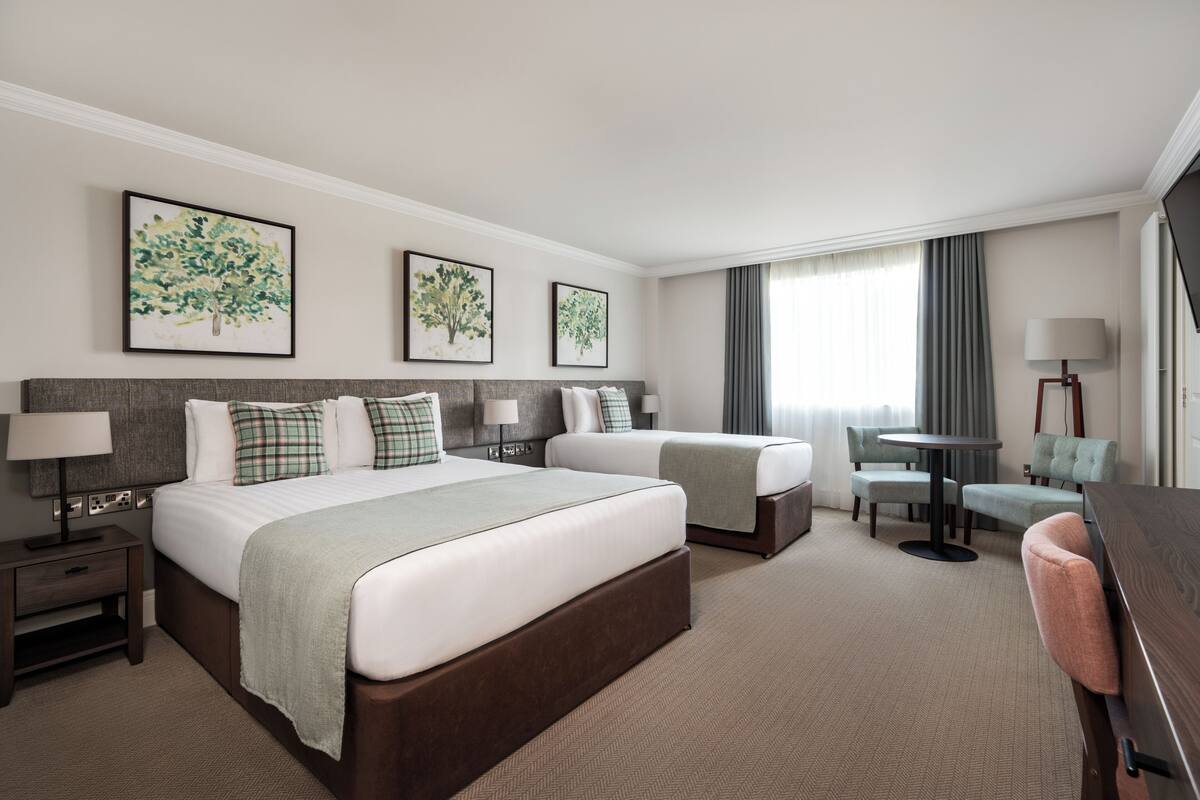 A hotel room with two beds, a desk, a chair, and artwork on the walls.