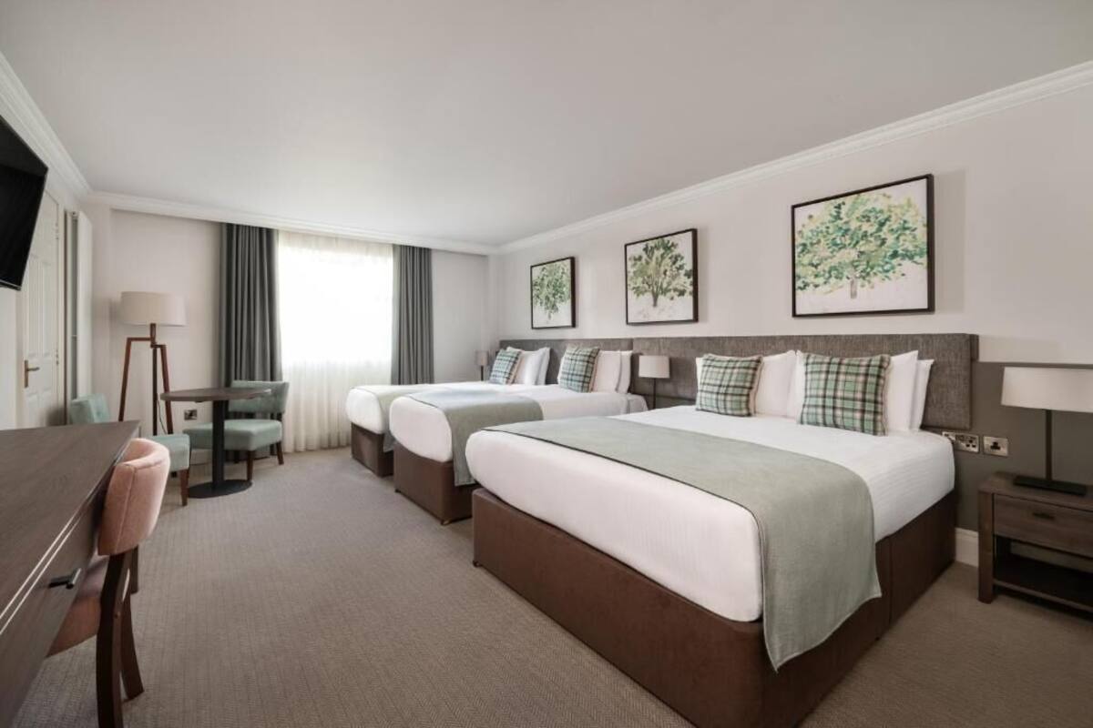 A hotel room with two beds, a desk, a chair, and a TV.