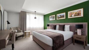 Quarto de hotel com uma cama grande, uma escrivaninha, uma cadeira, uma mesinha e um criado-mudo.