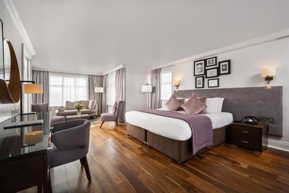 A modern hotel room with a large bed, a desk, a chair, and a sofa.