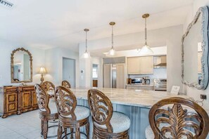A dining area with a marble island, wooden chairs, and pendant lighting.