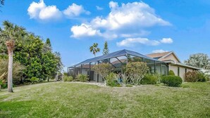 Een modern huis met een glazen oranjerie, omgeven door een verzorgd gazon en diverse bomen.