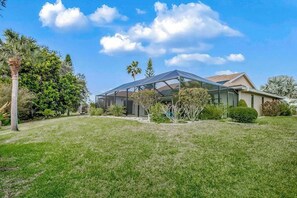 A modern house with a glass conservatory, surrounded by a well-maintained lawn and various trees. - Canal-front home with sandy beaches, golf courses, dock, & refreshing pool (Rotonda West)