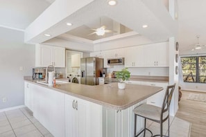 A modern kitchen with white cabinets, a central island, stainless steel appliances, and a ceiling fan. - Canal-front home with sandy beaches, golf courses, dock, & refreshing pool (Rotonda West)