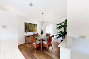 A dining area with a round table, wicker chairs, a chandelier, and a large plant. - Bohemian canal-front retreat with pool, beach gear, adult bikes, & AC - dogs ok (Rotonda West)
