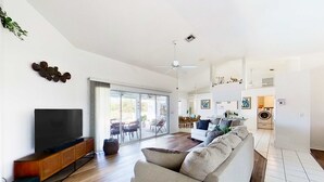 A spacious living area with a flat-screen TV, a sofa, a dining table, and a sliding glass door leading to an outdoor patio. - Bohemian canal-front retreat with pool, beach gear, adult bikes, & AC - dogs ok (Rotonda West)
