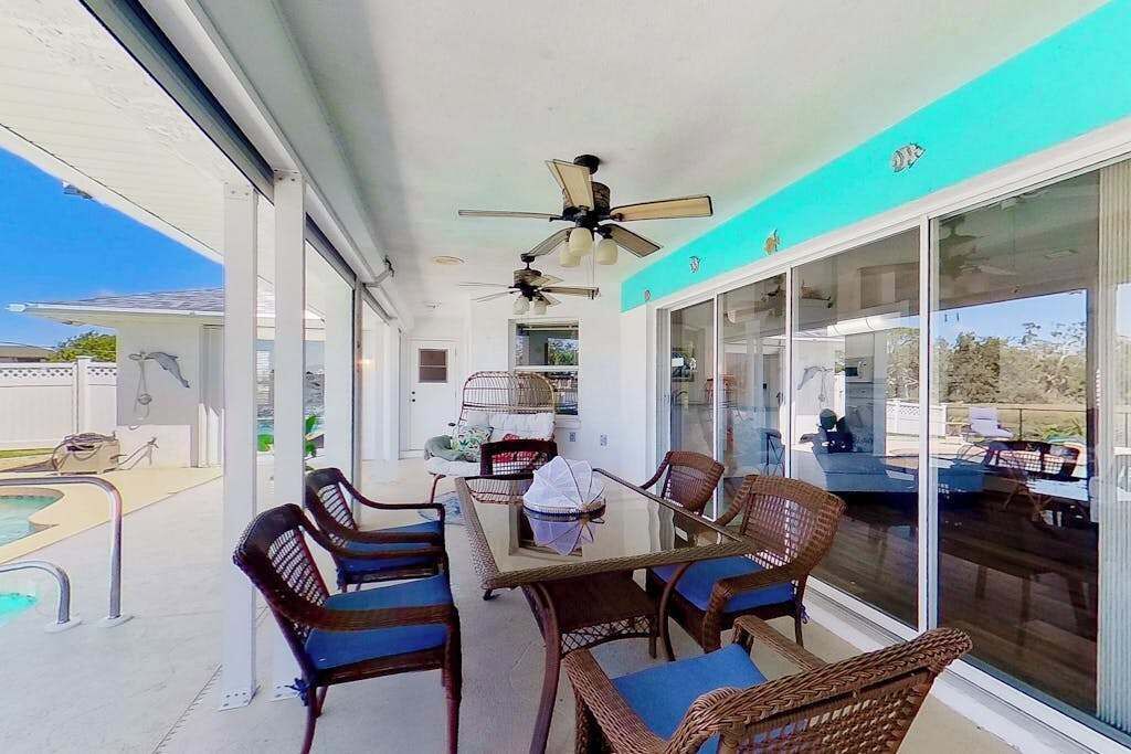 Eine überdachte Terrasse mit Pool, Korbmöbeln, Deckenventilatoren und großen Schiebetüren.