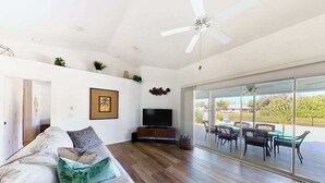 A modern living room with a sofa, television, and a dining area with chairs and a table. - Bohemian canal-front retreat with pool, beach gear, adult bikes, & AC - dogs ok (Rotonda West)
