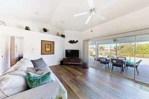 A modern living room with a sofa, television, and a dining area with chairs and a table. - Bohemian canal-front retreat with pool, beach gear, adult bikes, & AC - dogs ok (Rotonda West)