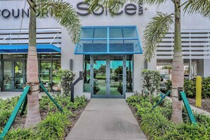 A building entrance with a blue awning, palm trees, and a pathway leading to the door. - Exceptional condo with balcony, WIFi, and located close to beaches and downtown (Naples)