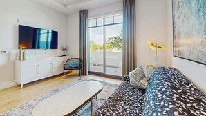 A modern living room with a sofa, a TV, a dining table, and a view of the outdoors. - Exceptional condo with balcony, WIFi, and located close to beaches and downtown (Naples)