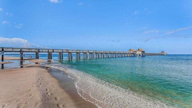 A beach with a wooden pier extending into the water, a sandy shore, and clear blue skies. - Exceptional condo with balcony, WIFi, and located close to beaches and downtown (Naples)