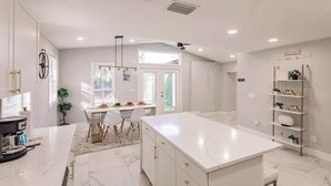 A modern kitchen with white cabinetry, a large island, and a dining area with chairs and a table. - Spacious home private heated pool, fireplace, & two kitchens-near downtown (Naples)